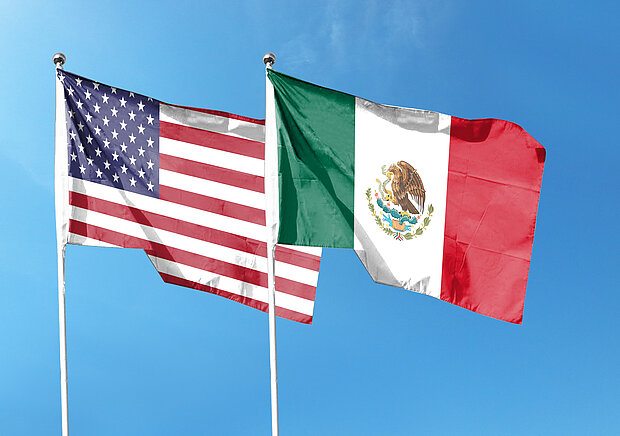 Two flags waving, one from the United States and one from Mexico